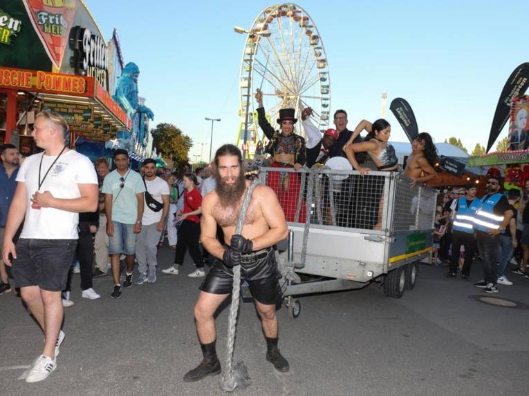 Ein Mann, der einen Wagen voller Artist*inne zieht.